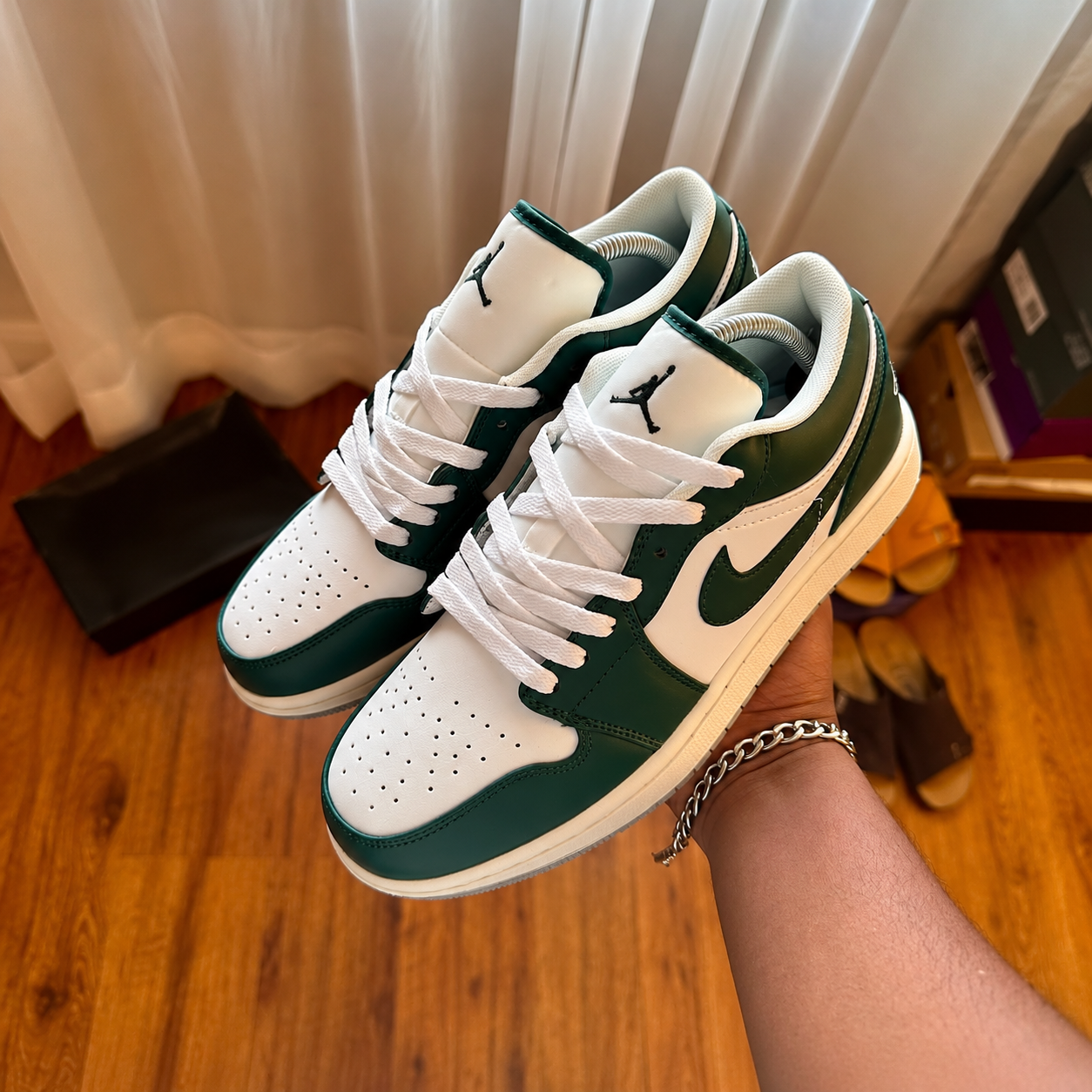 Forest green and white Jordan 1 Low sneakers held in hand